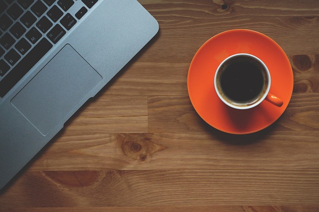 A cup of coffee next to a laptop on a lunch cooler bag.