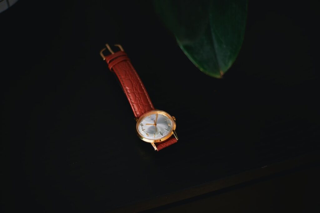 A gold watch with a leather wrist watch strap on a black table next to a plant.