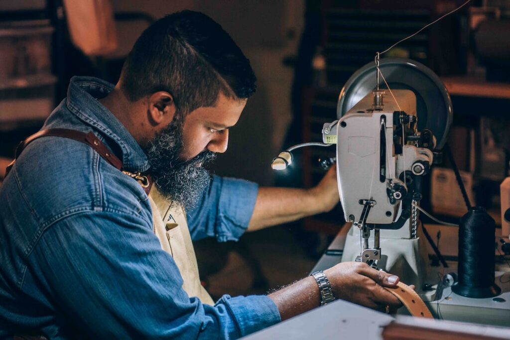 A man crafting high-quality leather bags for men on a sewing machine.