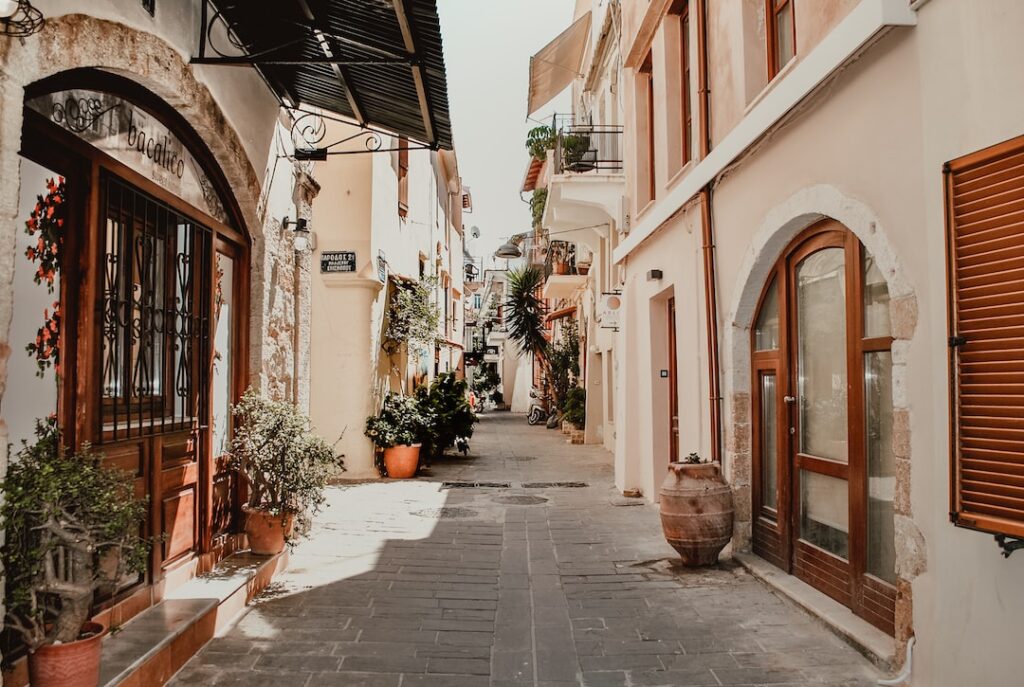 A narrow street lined with buildings and potted plants, featuring an attache case.