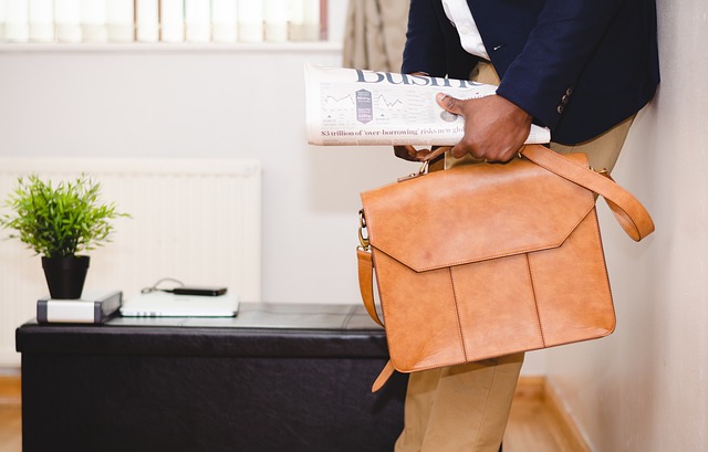 A man holding an attache case and reading a newspaper.