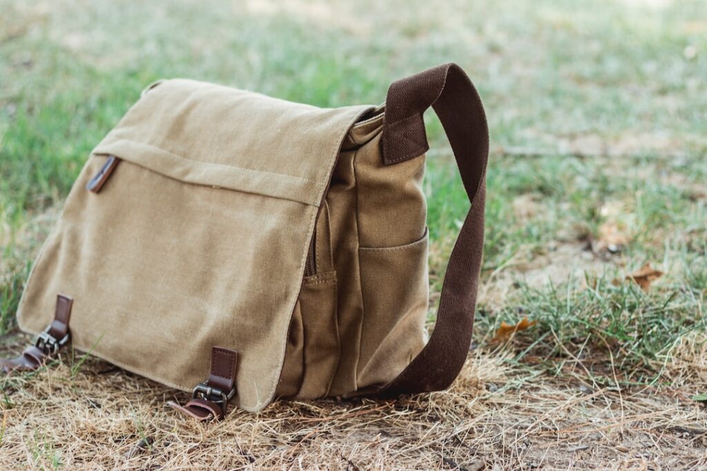 A perfect tan canvas messenger bag sitting in the grass.