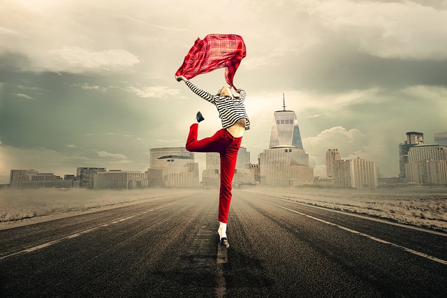 A woman gracefully dances on a road, twirling a red scarf while carrying a small crossbody bag.