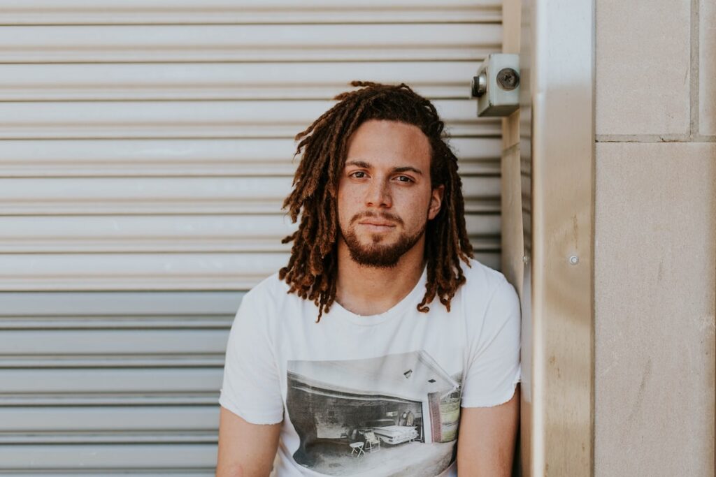 A first-rate man with dreadlocks sitting in front of a garage.