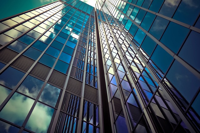 A striking low-angle shot of a modern glass skyscraper, its sleek reflective windows patterning the sky with lines and angles, embodying urban sophistication.