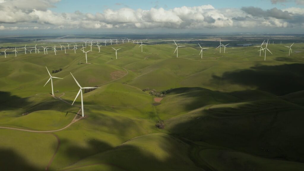 Aerial view of wind turbines elegantly dotted across rolling green hills. A symbol of sustainable fashion, harnessing nature's power with style.