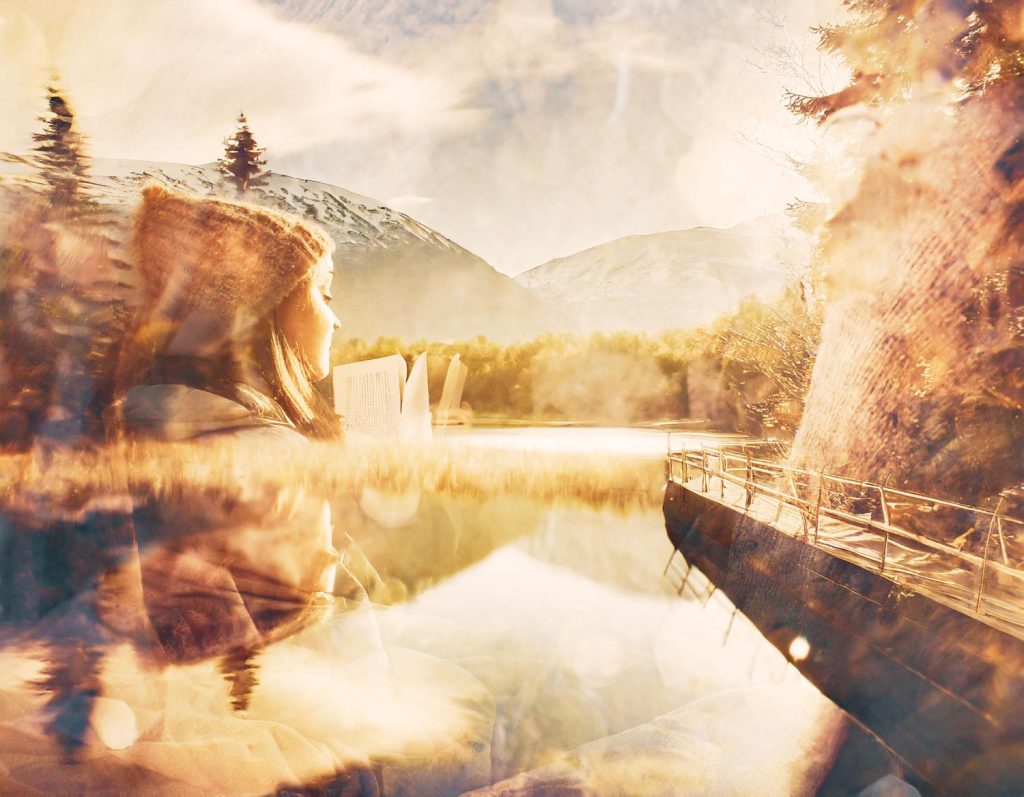 A stylish woman in a hat and retro sunglasses reads a book outdoors, set against a serene lakeside scene with snow-capped mountains and a sunlit dock.