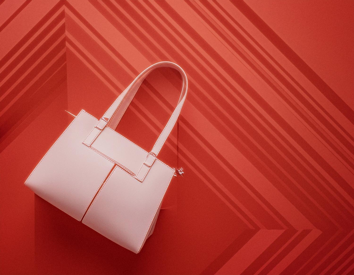 A chic white handbag with dual handles pops against a bold red geometric backdrop. Reminiscent of Gucci Neo Vintage, its minimalist design exudes timeless elegance.