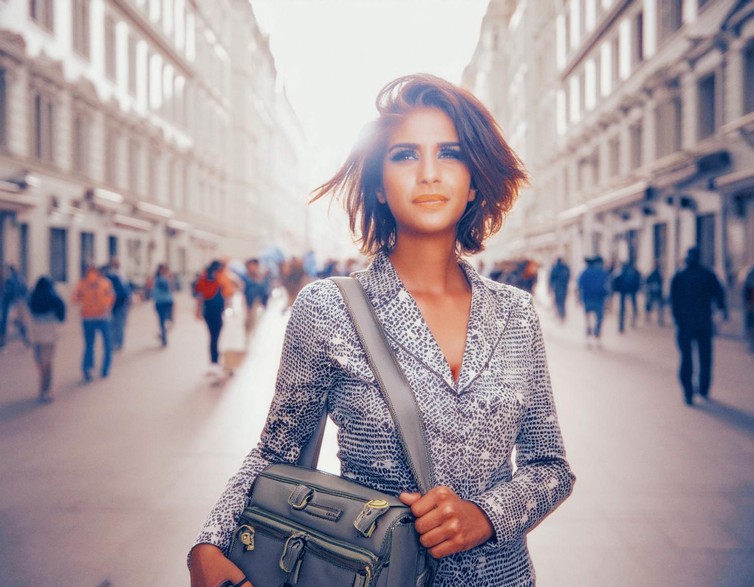 A confident woman with chic short hair stands on a bustling street, rocking a patterned blouse and grey leather messenger bag. Urban style at its best!