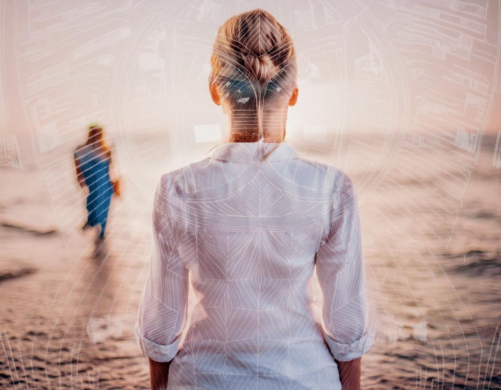 A person with a chic bun and light hair watches someone stylishly dressed in blue stroll along a sunset beach, framed by sleek geometric patterns from the Ultimate Incase A.R.C. Collection. #FashionInFocus #BeachStyle