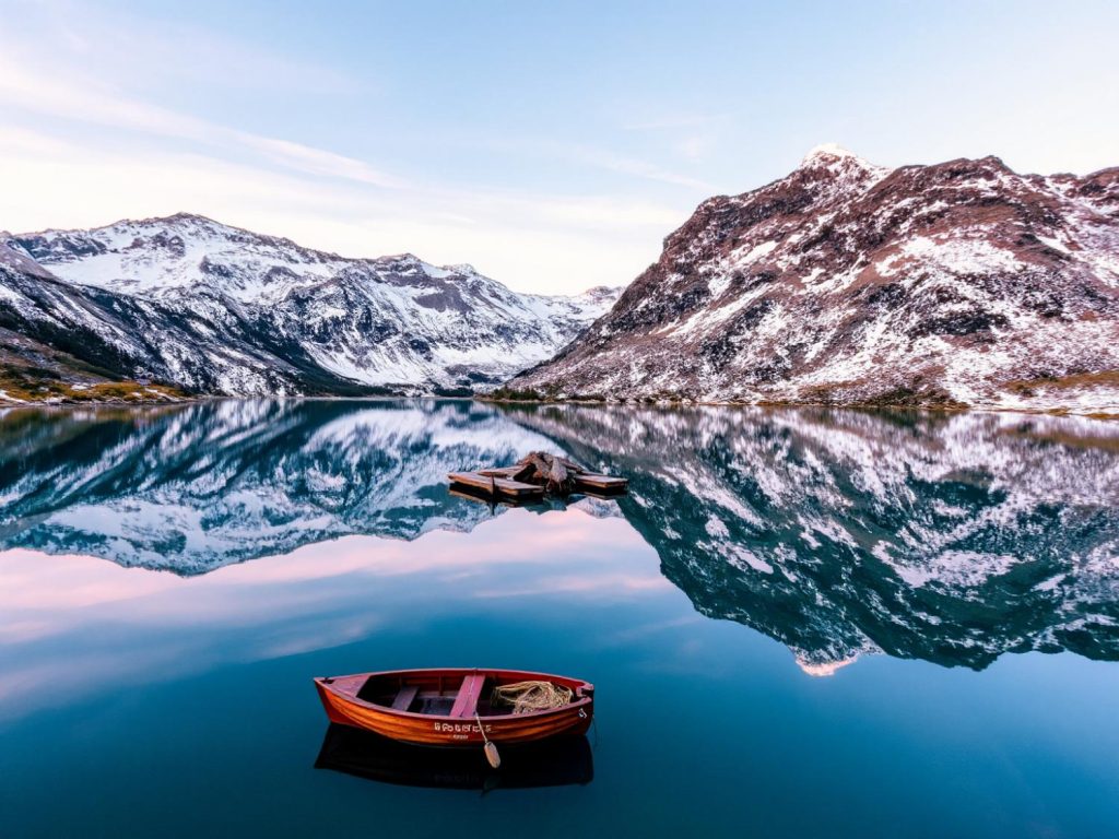 A serene lake reflects snow-capped peaks, a red boat adds a pop of color—perfect for travel-inspired fashion accessories.