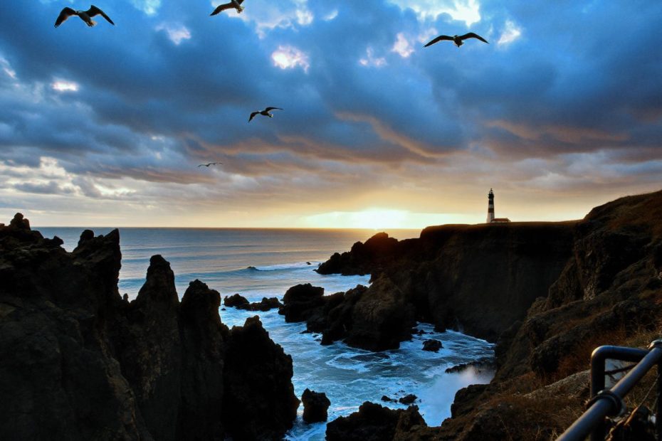 A sunset coastal scene with cliffs, a glowing horizon, and guiding lighthouse. A timeless blend of nature's drama and nautical-inspired style.