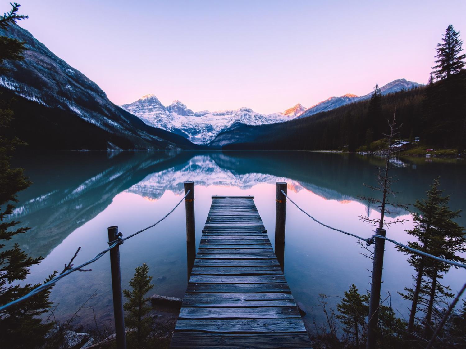 Wooden dock meets a tranquil lake, reflecting snow-capped peaks at sunrise. Nature's color palette inspires ethereal spring fashion hues.